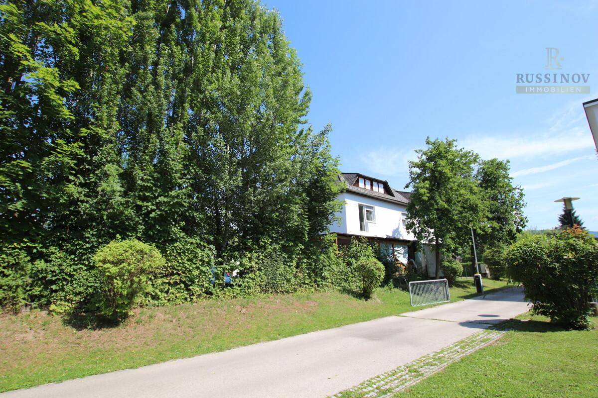 Weitläufige Grünfläche mit einem Weg und hohen Bäumen, im Hintergrund ist ein Gebäude sichtbar.