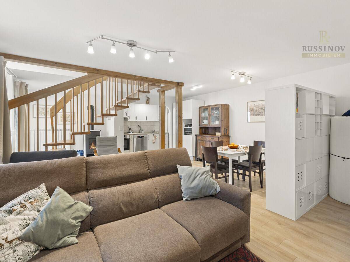 Gemütlicher Wohnbereich mit Sofa, Holzboden und offenem Übergang zum Ess- und Küchenbereich.