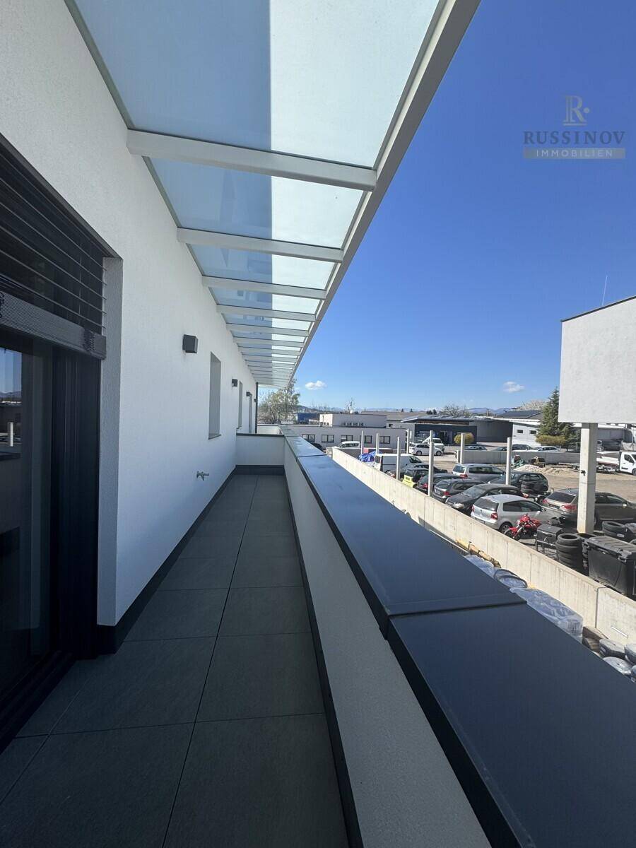 Langer, schmaler Balkon mit Glasüberdachung und Blick auf die Umgebung.