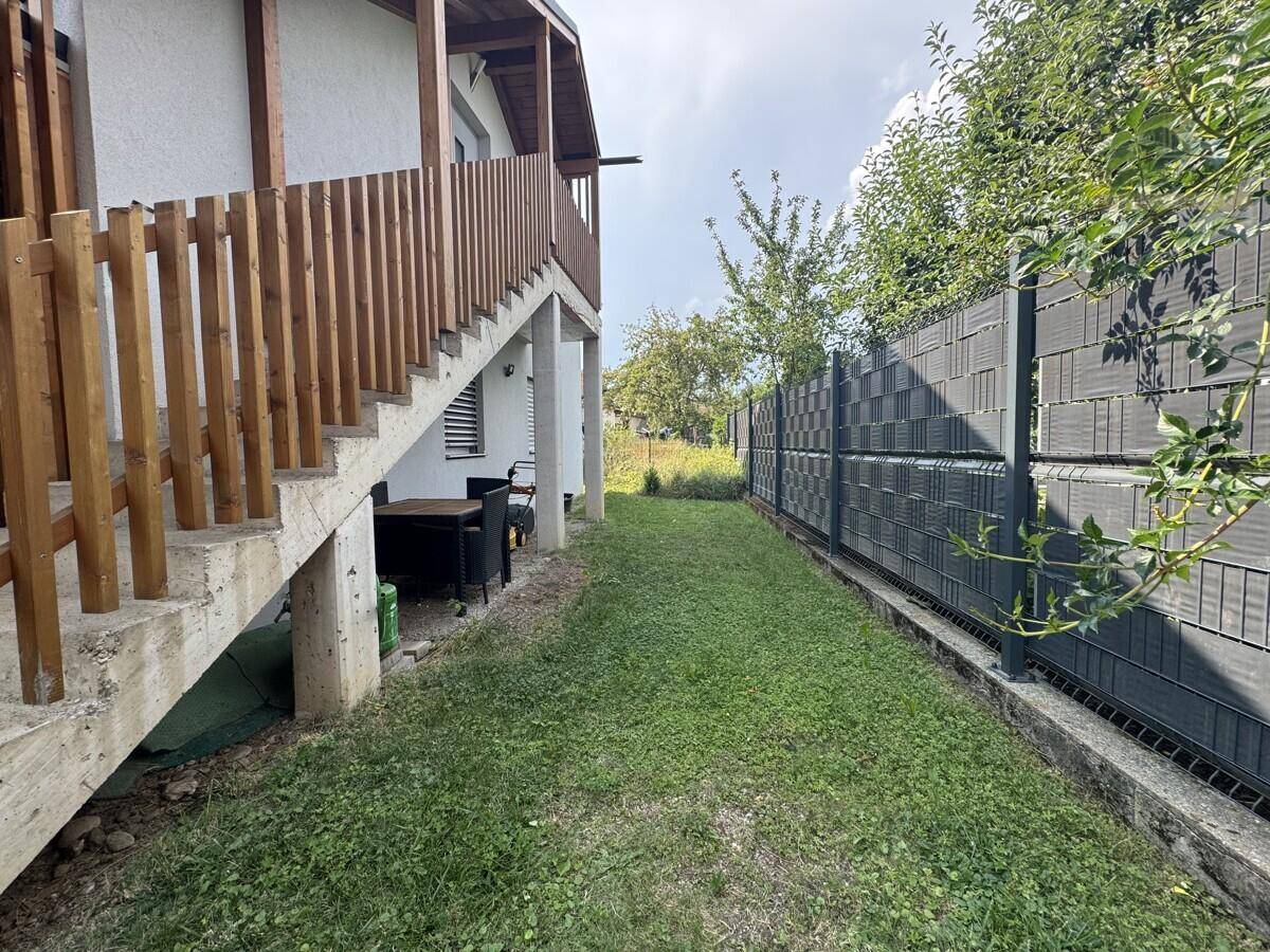 Grüner Gartenbereich neben dem Haus mit Außentreppe und einem Zaun.