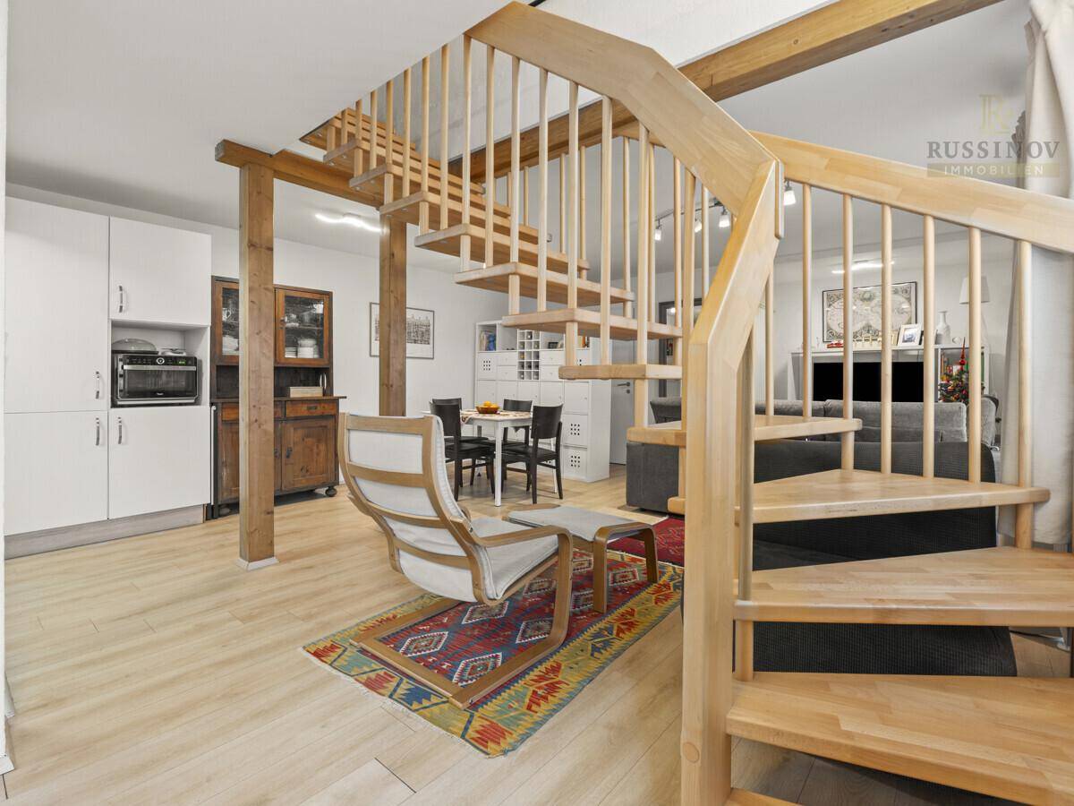 Offener Wohn- und Essbereich mit Holztreppe, Holzbalken und Blick auf den Essbereich.