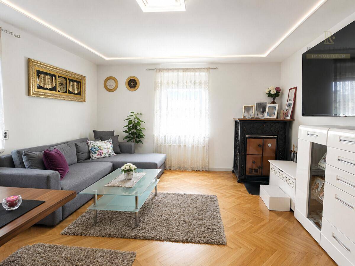 Helles Wohnzimmer mit Parkettboden, großem Sofa und einem traditionellen Kaminofen.