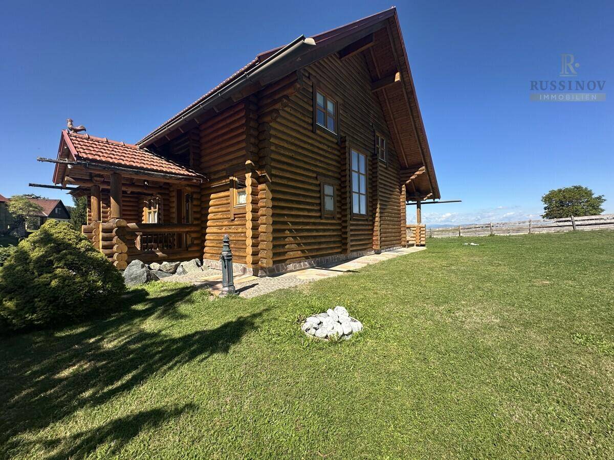 Rustikales Holzhaus mit weitläufigem Rasen und ländlicher Umgebung unter strahlend blauem Himmel.