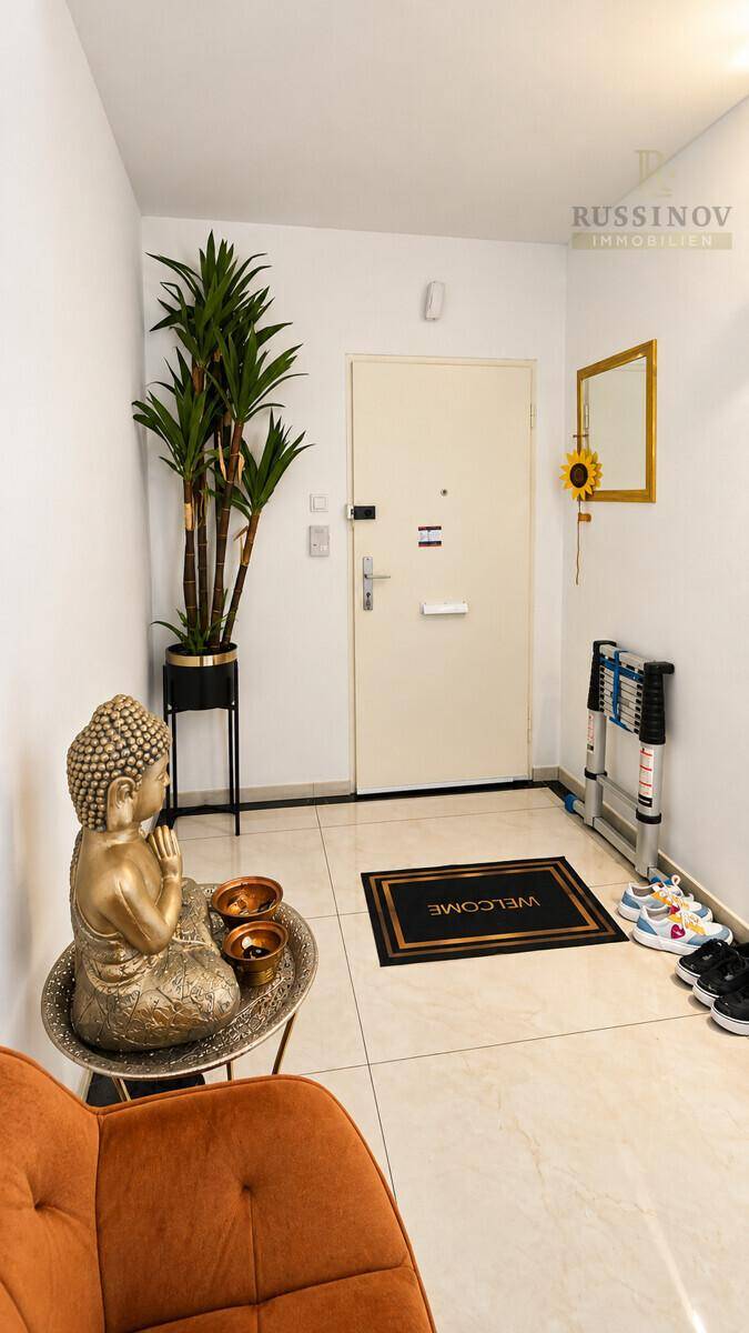 Heller Eingangsbereich mit weißer Tür, Schuhregal und dekorativer Buddha-Statue.