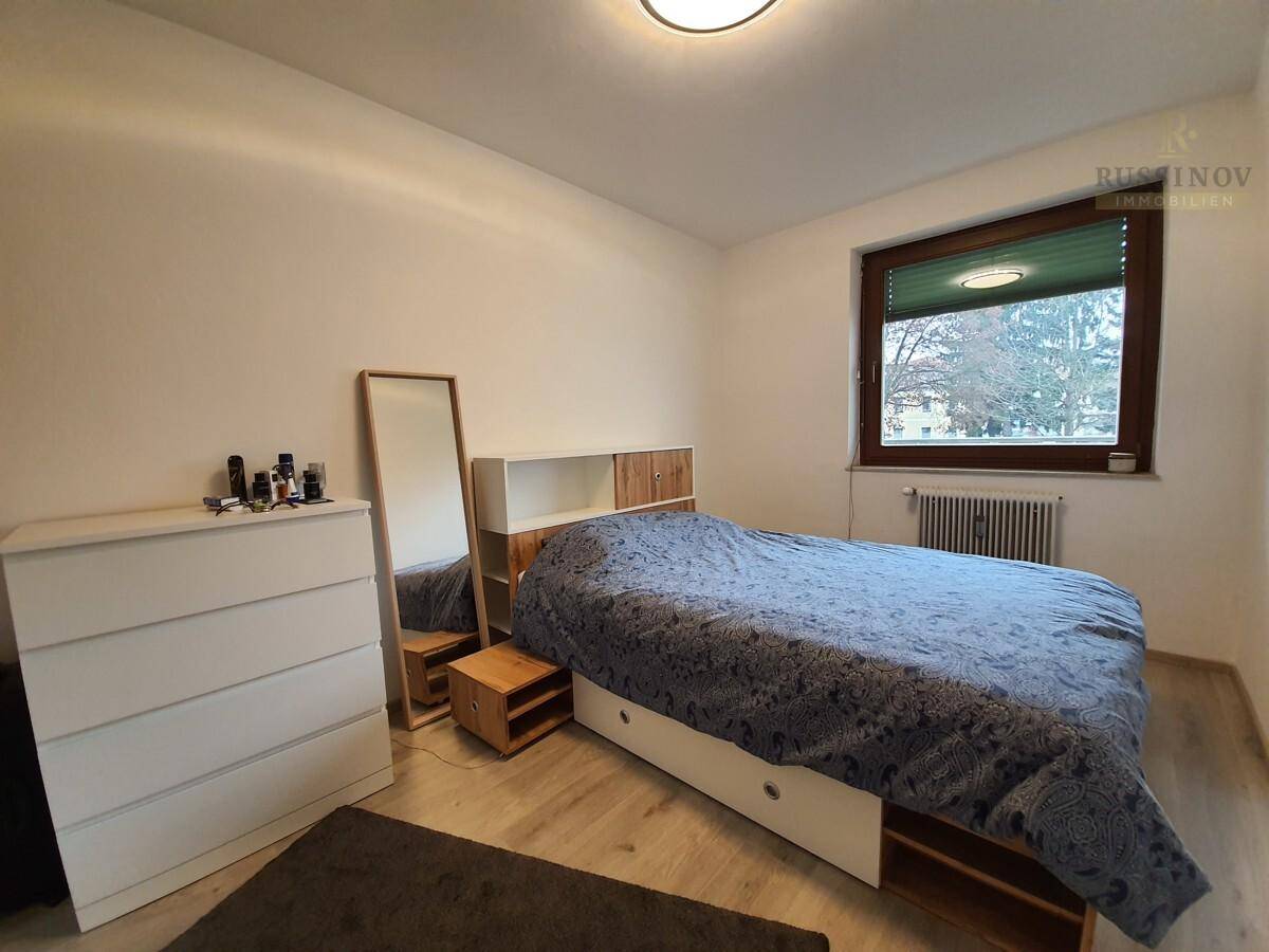 Schlafzimmer mit Doppelbett, Kommode, Spiegel und Fenster.
