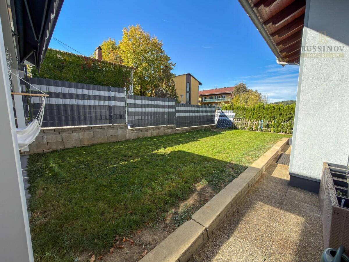 Gepflegter Gartenbereich mit Rasenfläche, Zaun und sonniger Ausrichtung.