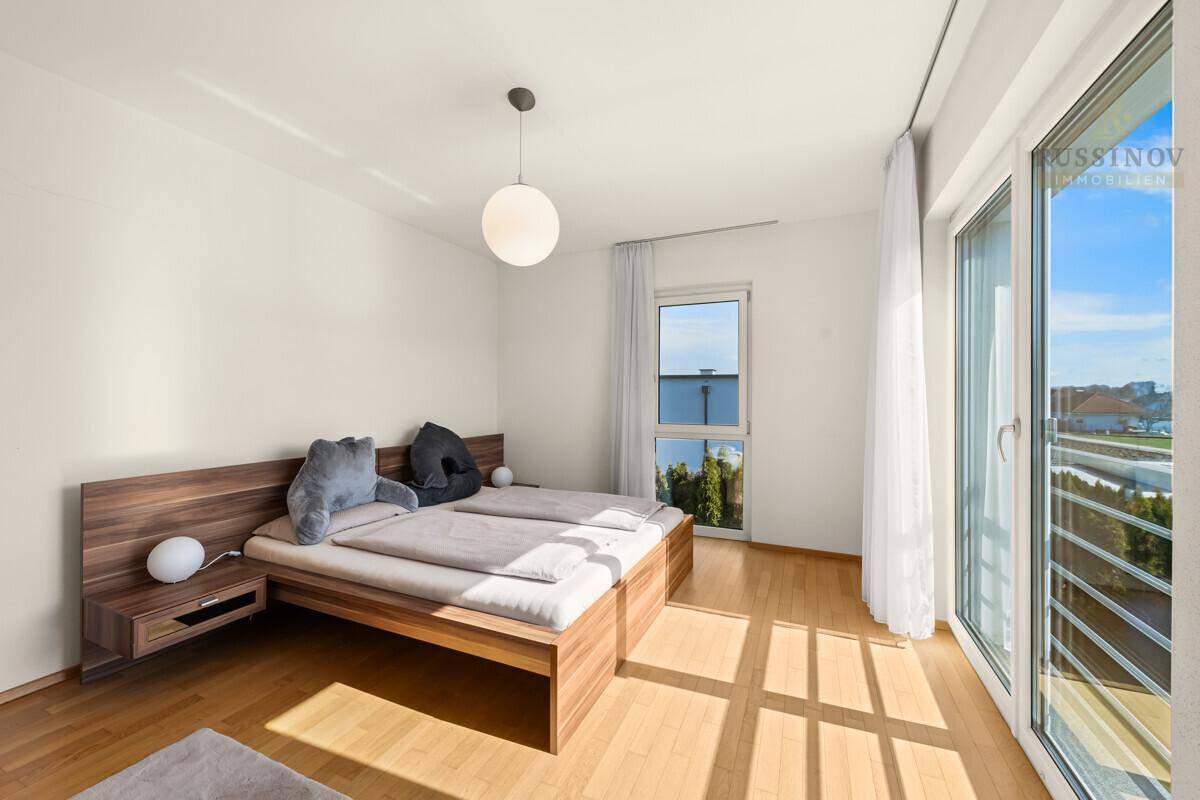 Helles Schlafzimmer mit Holzbett, Parkettboden und Balkonzugang.