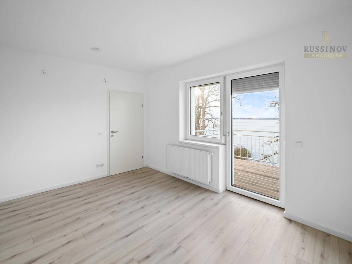 Helles, leeres Zimmer mit Laminatboden und Zugang zu einem Balkon, bietet viel Tageslicht.