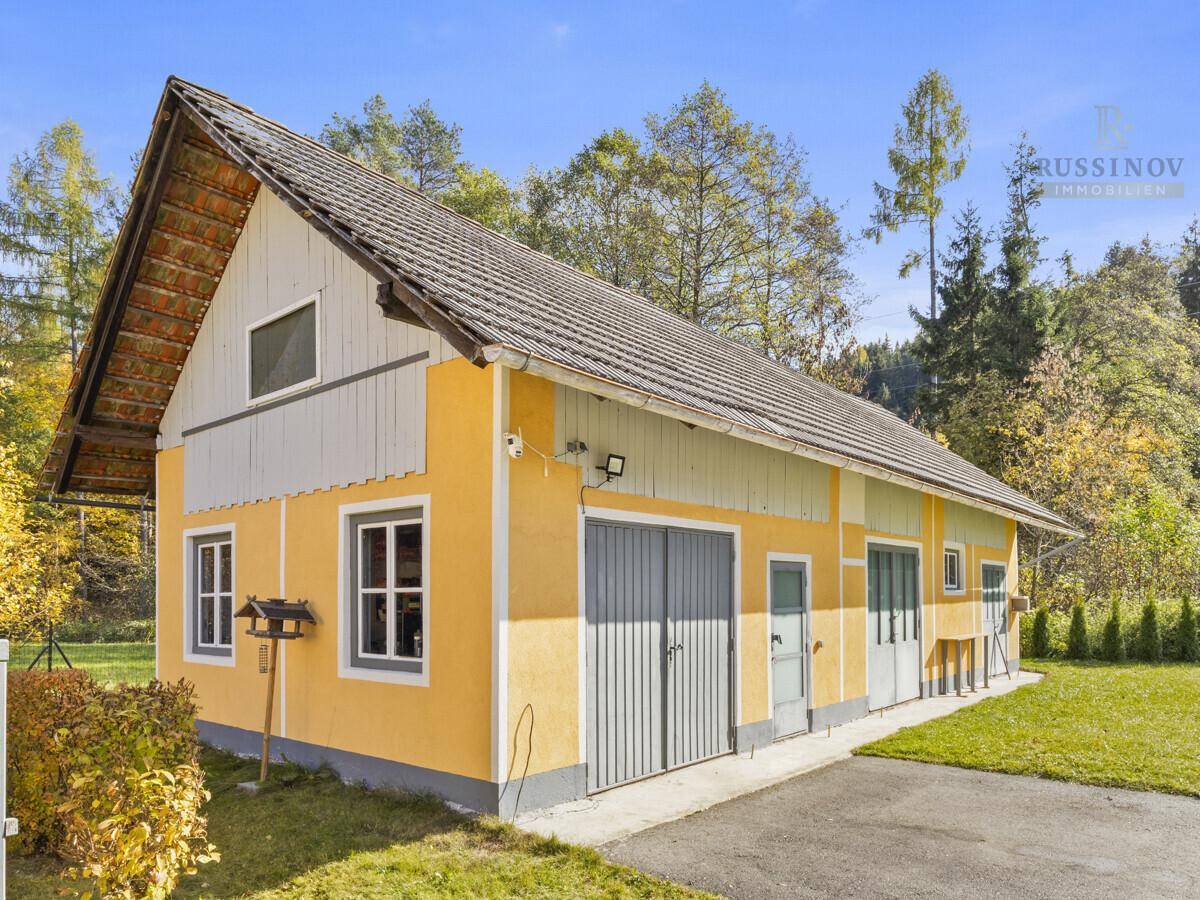 Gelbes Nebengebäude mit Satteldach und Garagentoren auf einem grünen Grundstück.
