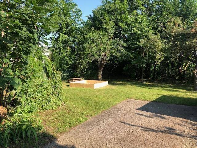 Grüner Gartenbereich mit Rasenfläche, Bäumen und einem Sandkasten, ideal für Kinder.