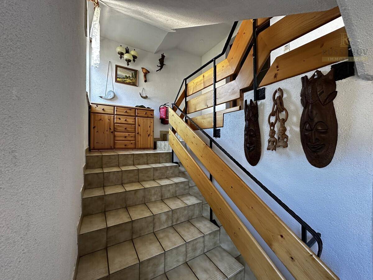 Treppenhaus mit Holzgeländer, Fliesenstufen und rustikalen Dekorationselementen an der Wand.