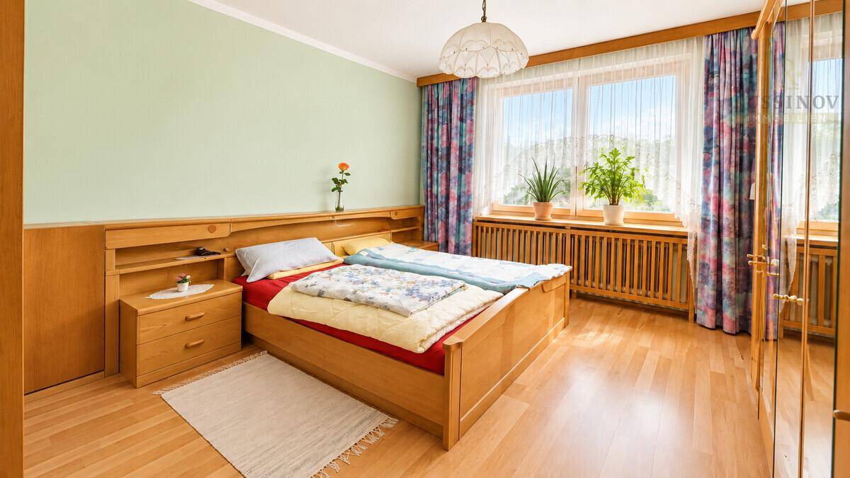 Gemütliches Schlafzimmer mit Holzmöbeln, Parkettboden und einem großen Fenster mit Blick ins Grüne.