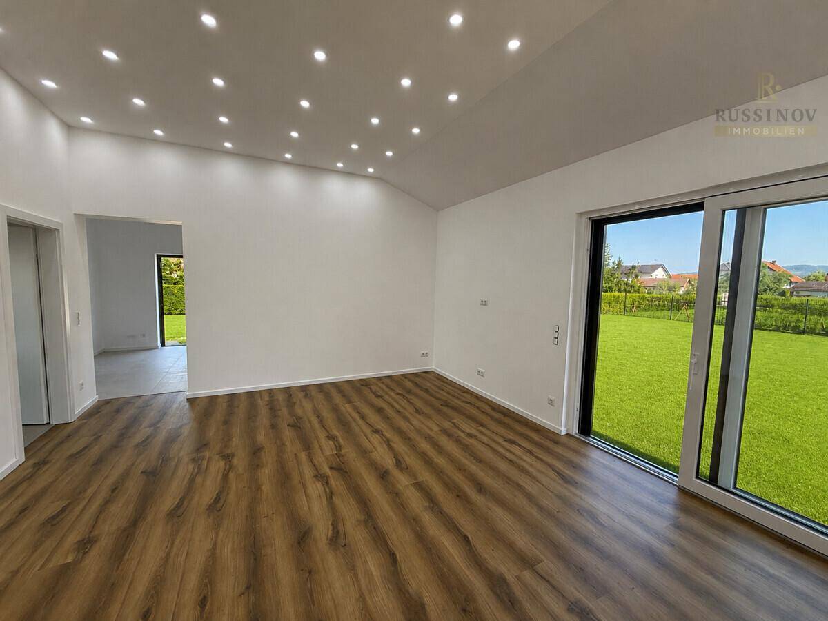 Heller Wohnbereich mit modernem Laminatboden, vielen Deckenspots und Zugang zum Garten.