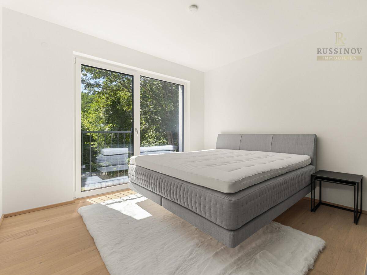 Helles Schlafzimmer mit großem Bett, Holzboden und französischem Balkon mit Blick ins Grüne.