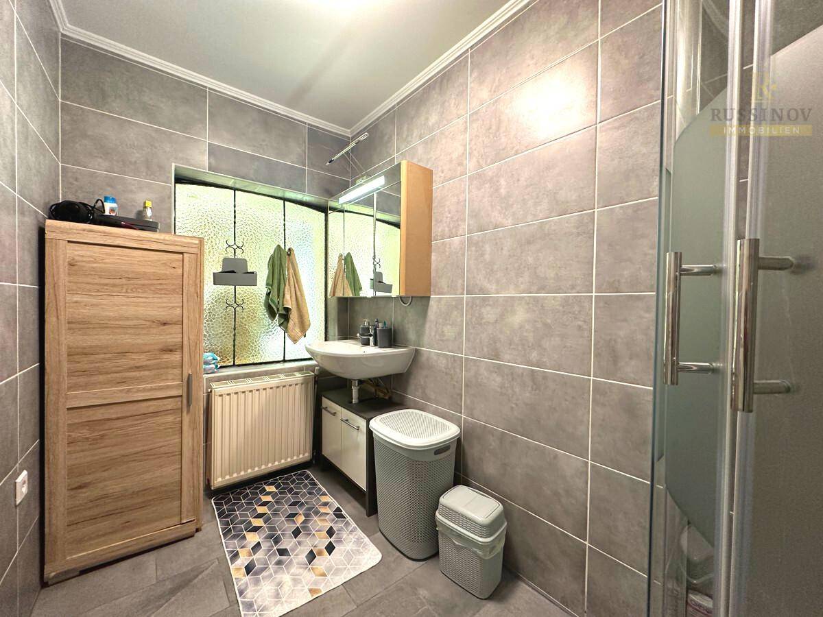 Modern gefliestes Badezimmer mit Dusche, Waschbecken und Fenster für Tageslicht.