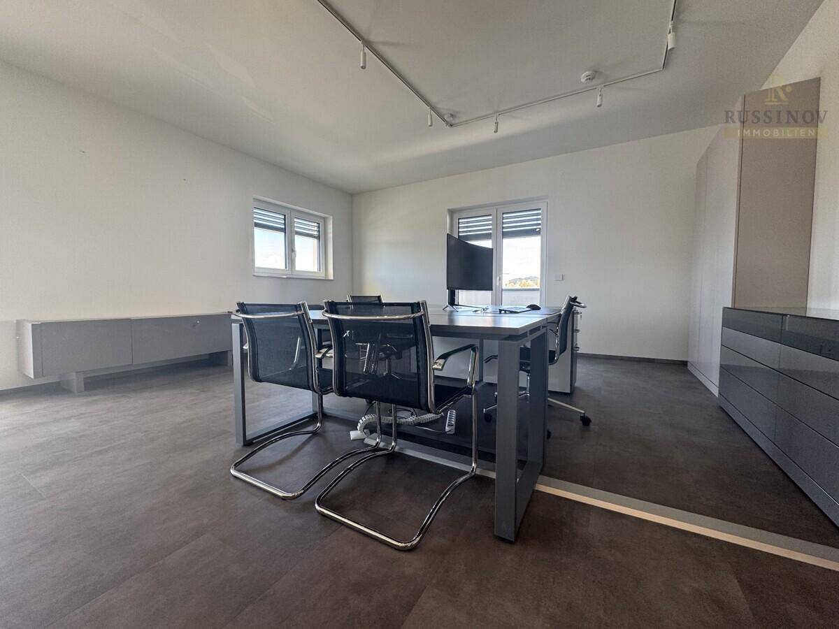 Modern eingerichtetes Büro mit dunklem Schreibtisch, Bürostühlen und grauem Fliesenboden, ideal für Besprechungen.