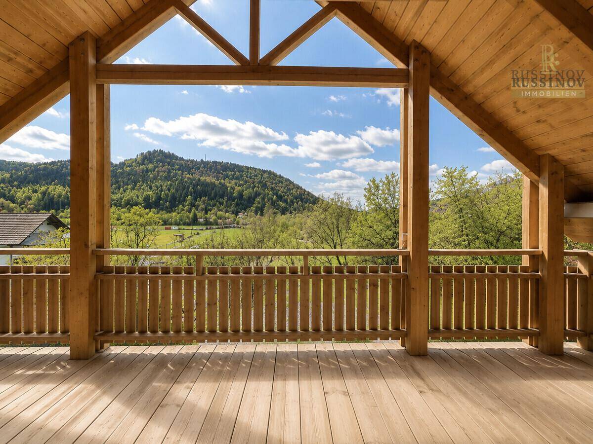 Geräumige Holzloggia mit atemberaubendem Blick auf die grünen Berge und das Tal unter blauem Himmel.