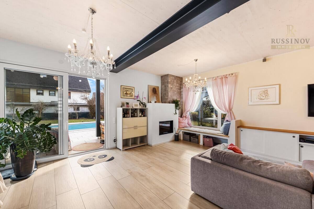 Lichtdurchfluteter Wohnbereich mit Zugang zum Außenbereich und Pool, ausgestattet mit modernem Kamin.