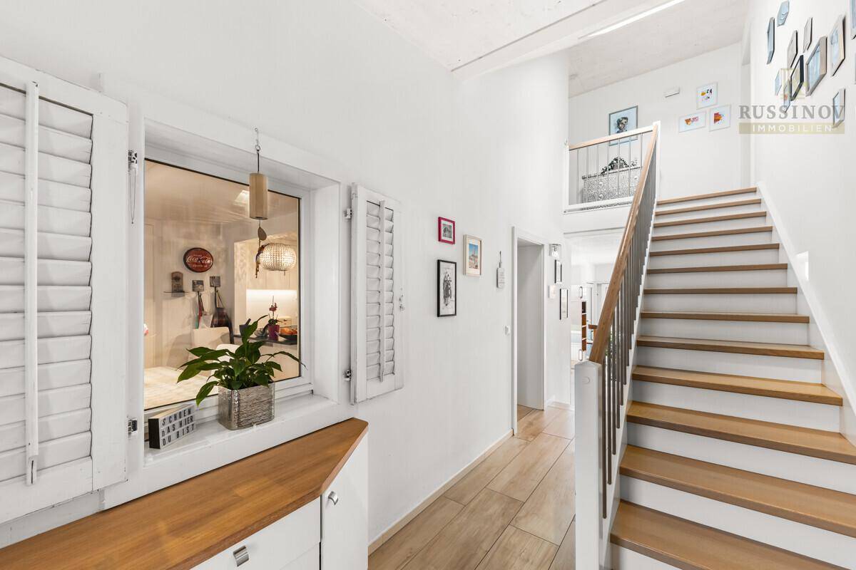 Heller Flur mit Holztreppe, Holzboden und Fenster mit weißen Fensterläden.