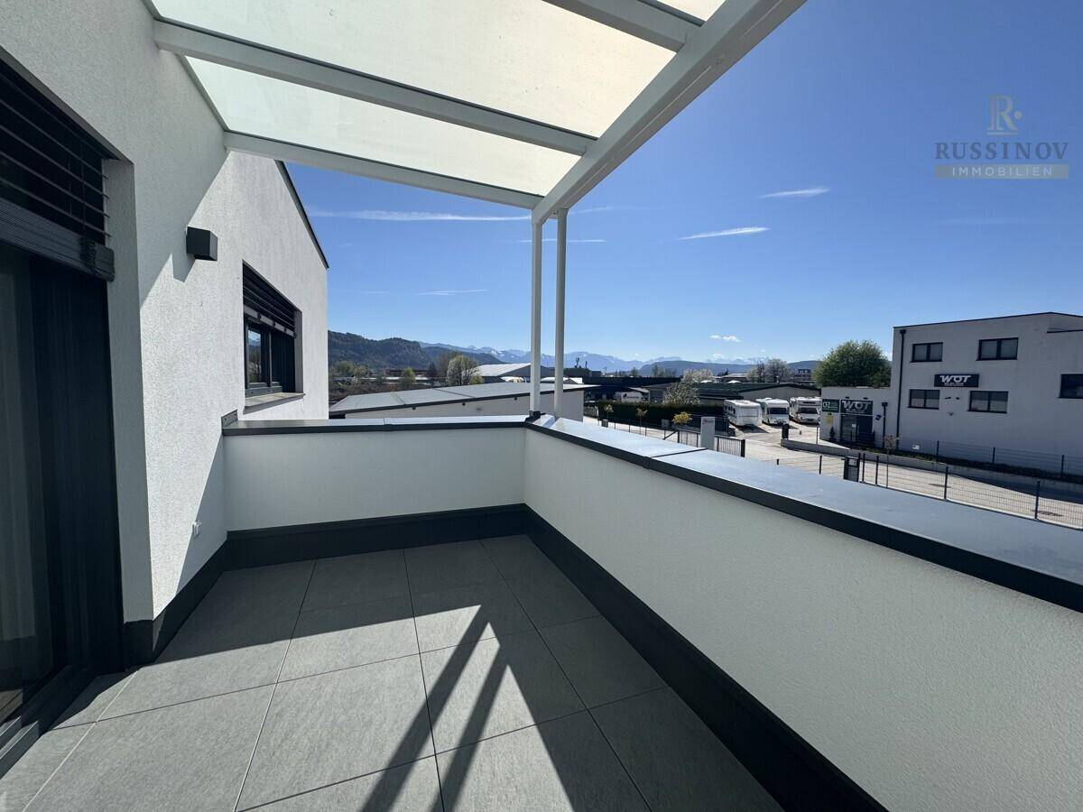Überdachter Balkon mit Fliesenboden und weitem Blick auf die umliegende Landschaft und Berge.