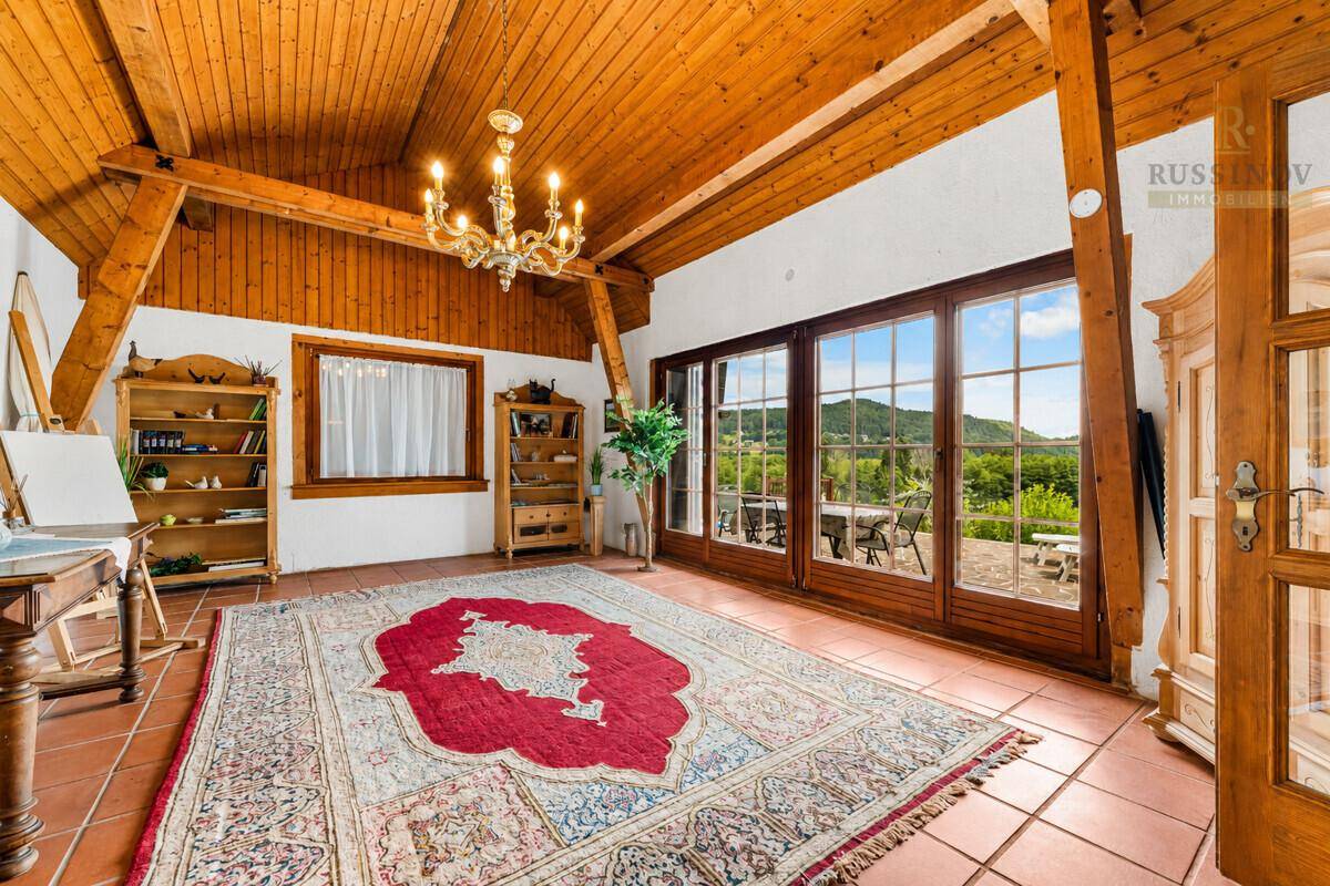 Helles Wohnzimmer mit Holzbalkendecke, Terrakottaboden und weitem Blick ins Grüne.