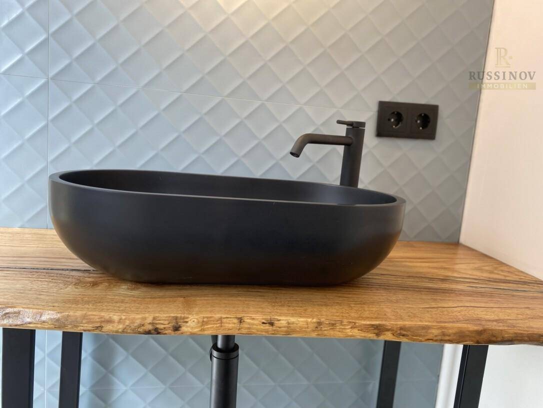 Modernes Badezimmer mit schwarzem Aufsatzwaschbecken und Holzwaschtisch auf hellblauen Fliesen.