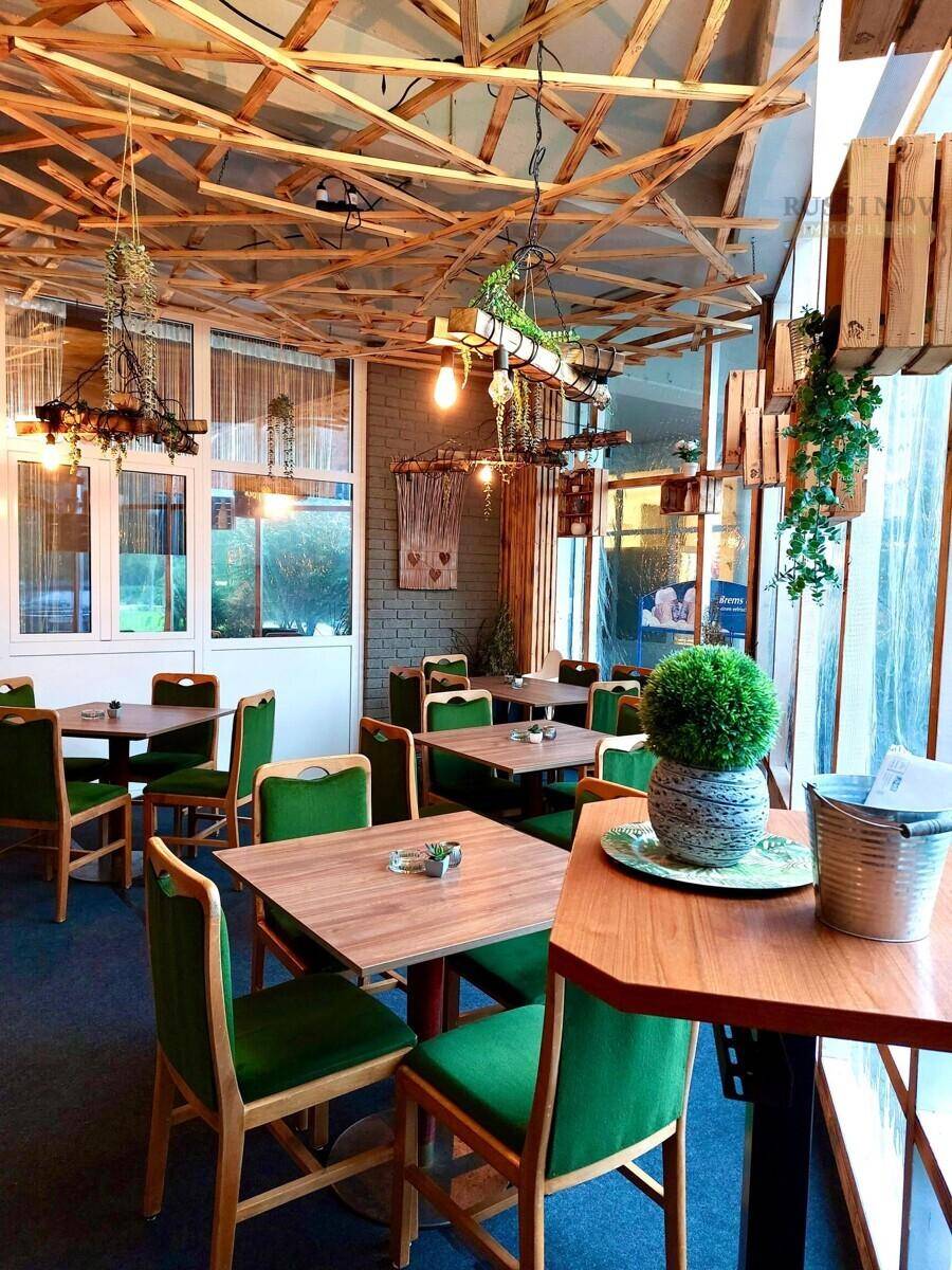 Gemütlicher Restaurantbereich mit Holztischen, grünen Stühlen und einer dekorativen Holzdeckenkonstruktion.