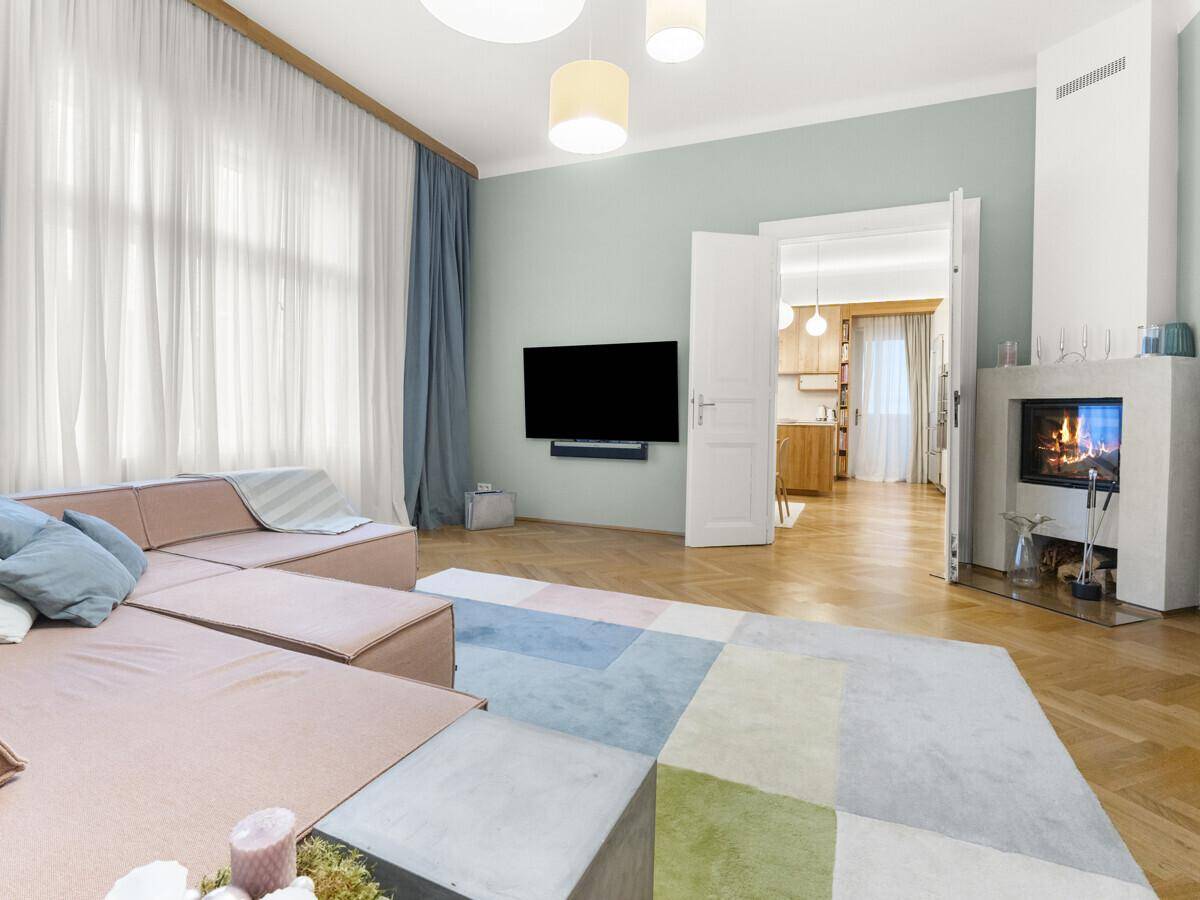 Helles Wohnzimmer mit modernem Kamin, Fischgrätparkett und Blick in die angrenzende Küche.