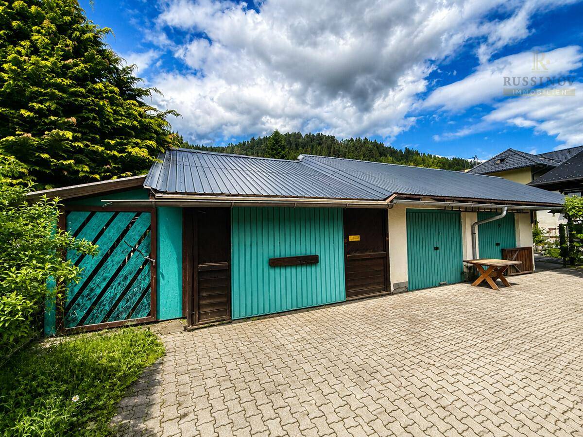Außenansicht eines Gebäudes mit mehreren Garagentoren in Türkis und gepflasterter Einfahrt.