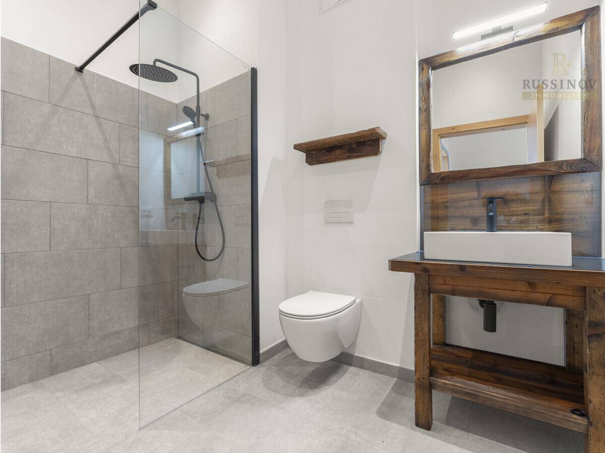 Modernes Badezimmer mit begehbarer Regendusche, Wand-WC und rustikalem Holzwaschtisch.
