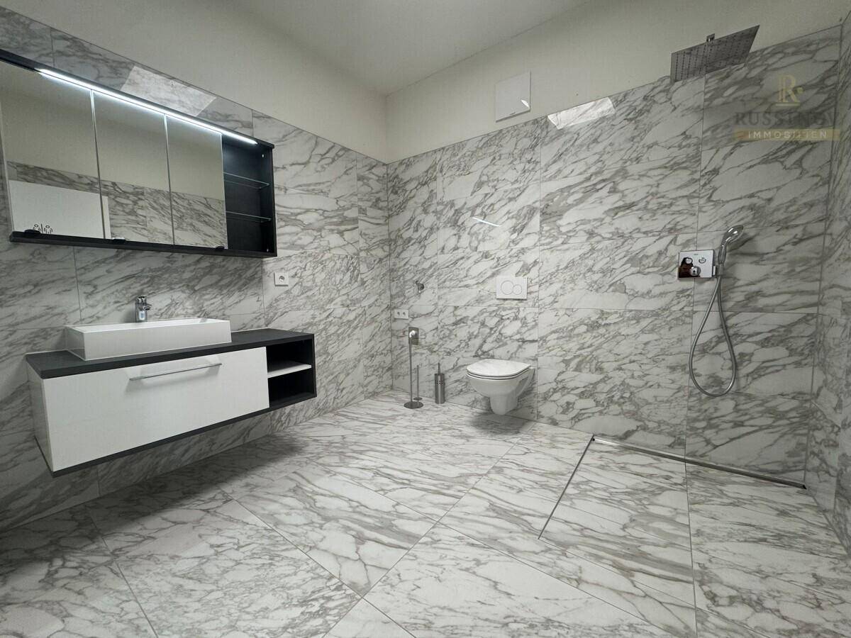 Modernes Badezimmer mit großformatigen Marmorfliesen, Dusche und Hänge-WC.