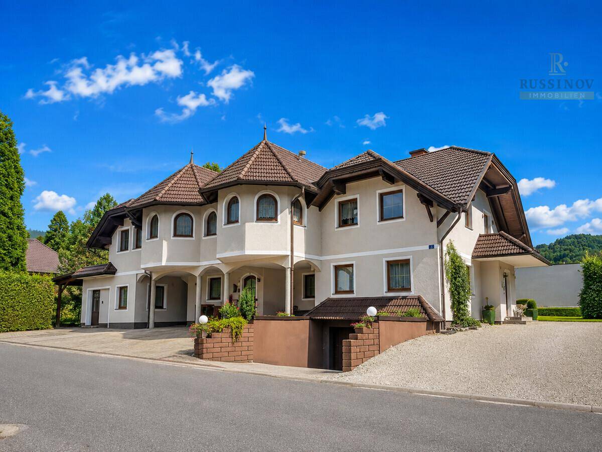 Gepflegtes Mehrfamilienhaus mit traditionellen Dächern und ausreichend Parkmöglichkeiten unter blauem Himmel.