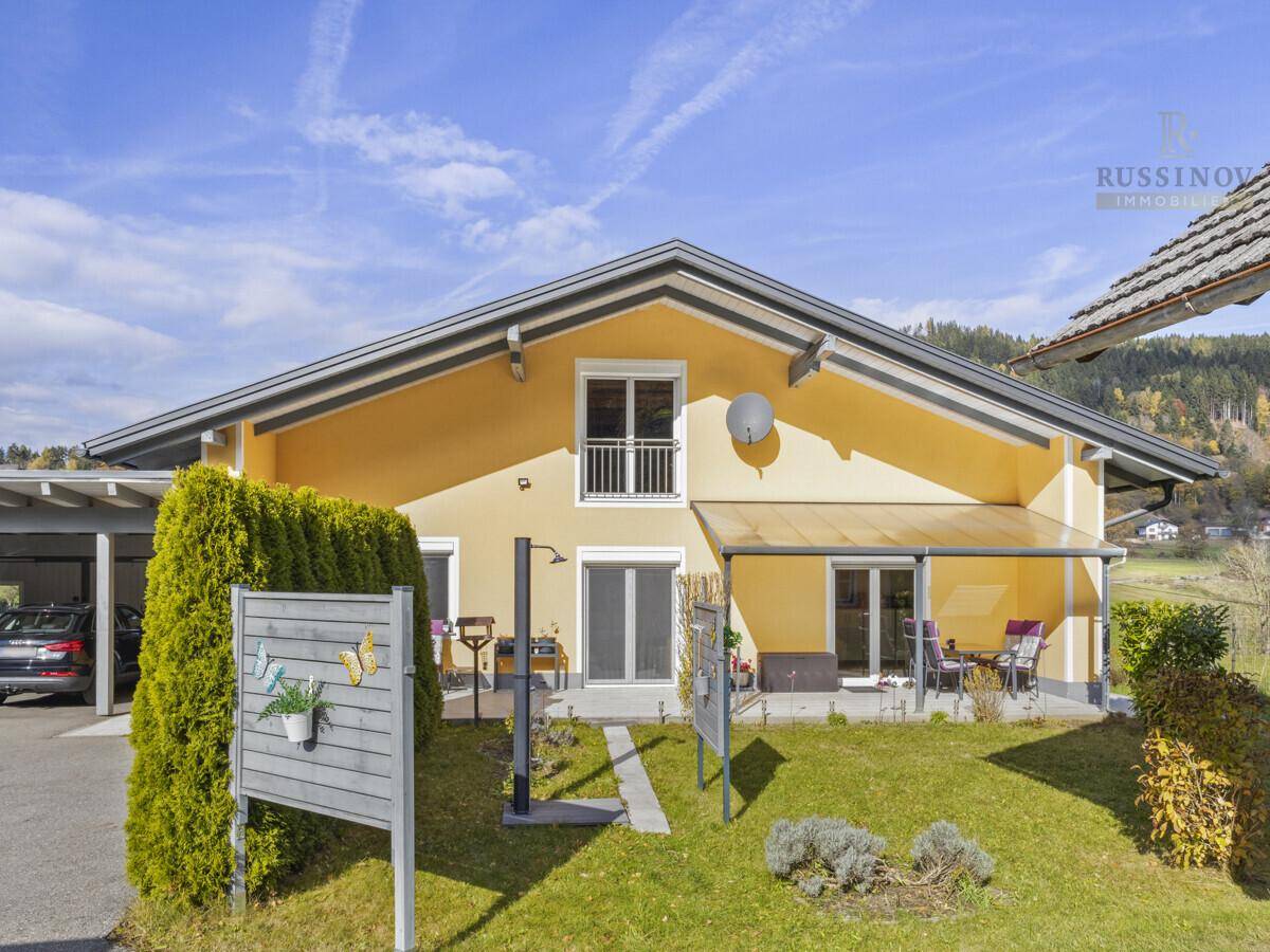 Rückseite des Hauses mit gepflegtem Rasen, überdachter Terrasse und kleinem Balkon.