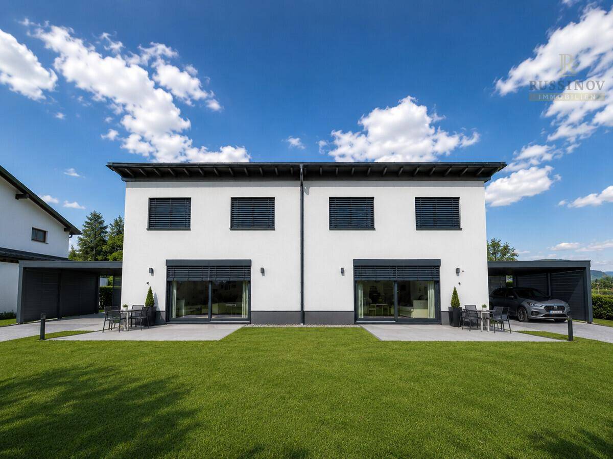 Moderne Doppelhaushälfte mit weißer Fassade, großen Fenstern, Rollläden und gepflegtem Rasen.