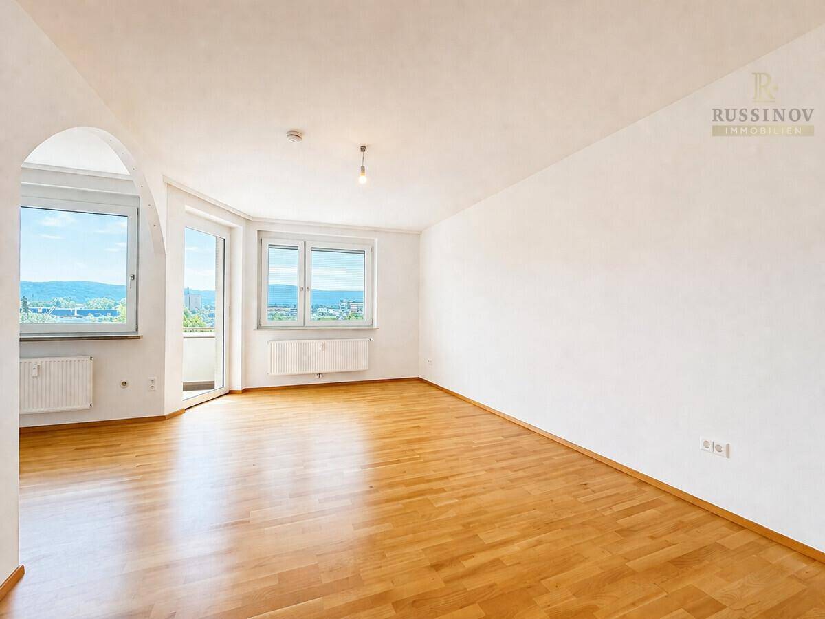 Heller Wohnraum mit Parkettboden, großen Fenstern und Zugang zum Balkon mit Weitblick.