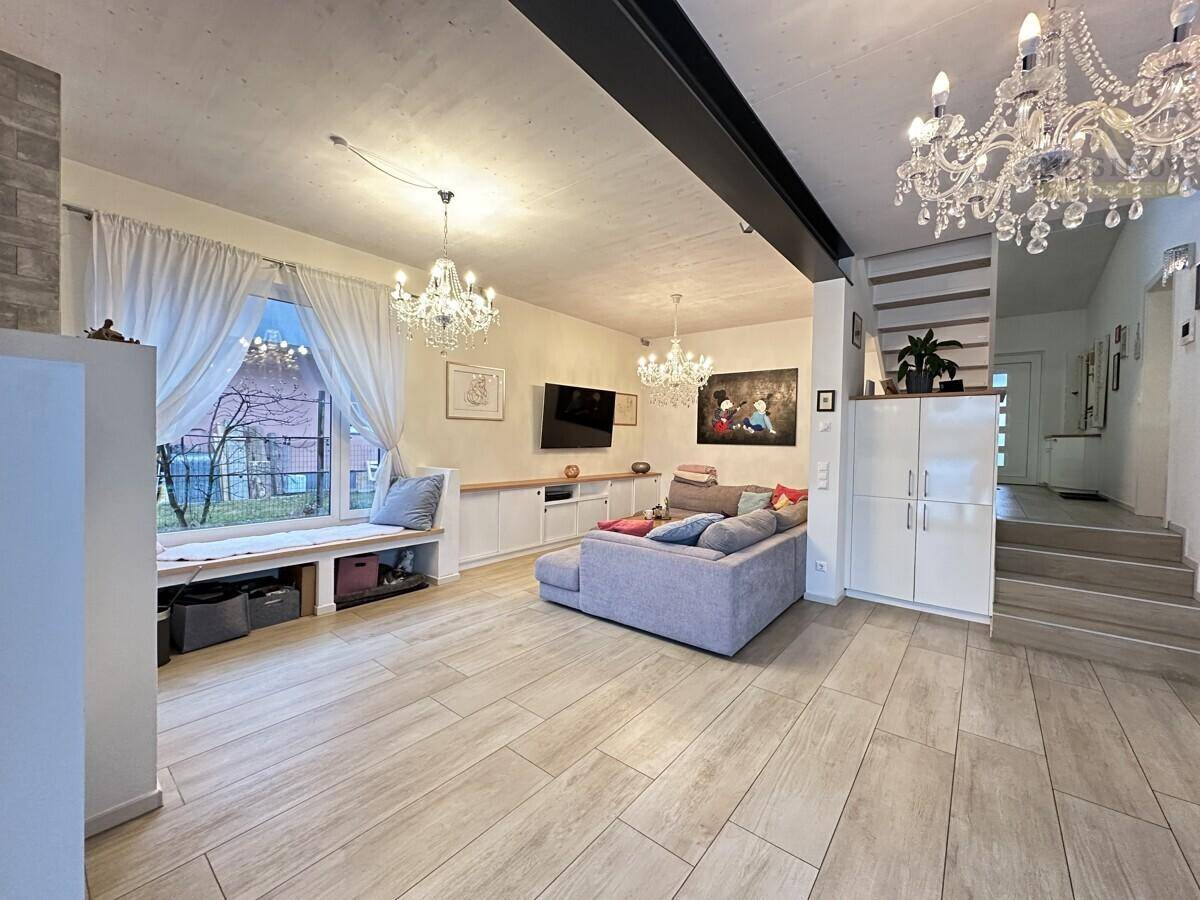 Geräumiger Wohnbereich mit hellem Fliesenboden, stilvollen Kronleuchtern und offenem Zugang zur Treppe.