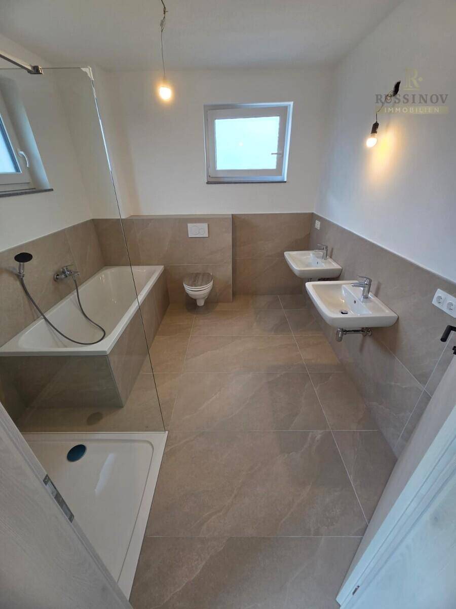 Modernes Badezimmer mit Doppelwaschbecken, Badewanne, Dusche und Fenster für Tageslicht.