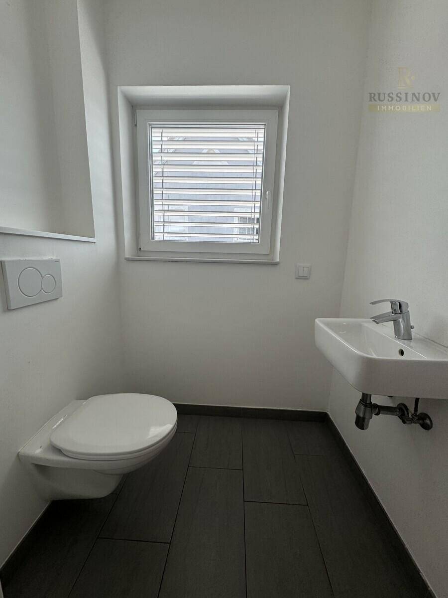 Kleines Gäste-WC mit wandhängender Toilette, Handwaschbecken und Fenster für natürliche Belüftung.