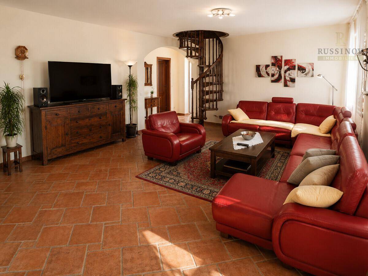 Gemütliches Wohnzimmer mit roten Ledersofas, Terrakottaboden und eleganter Wendeltreppe.