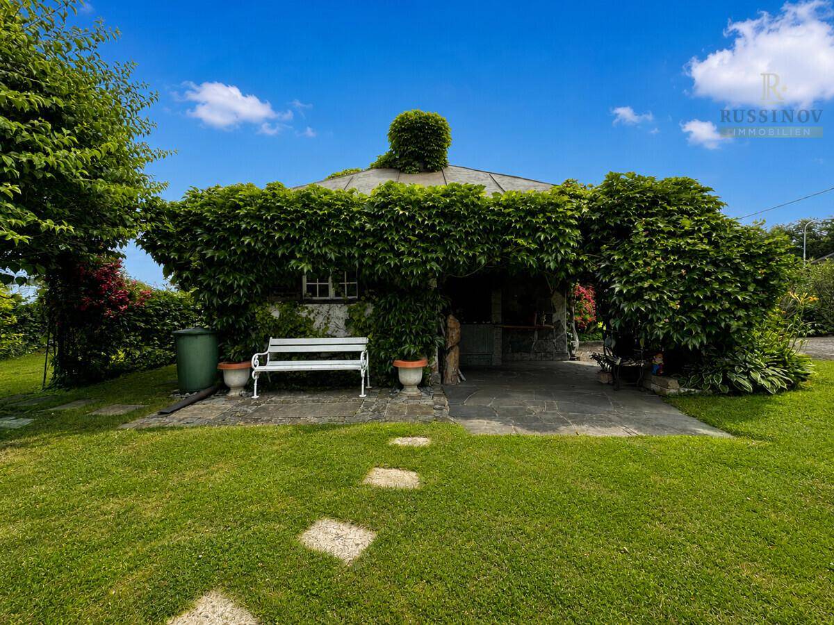 Idyllischer Gartenbereich mit üppiger Begrünung, Rasenfläche und einer überwachsenen Gartenlaube.