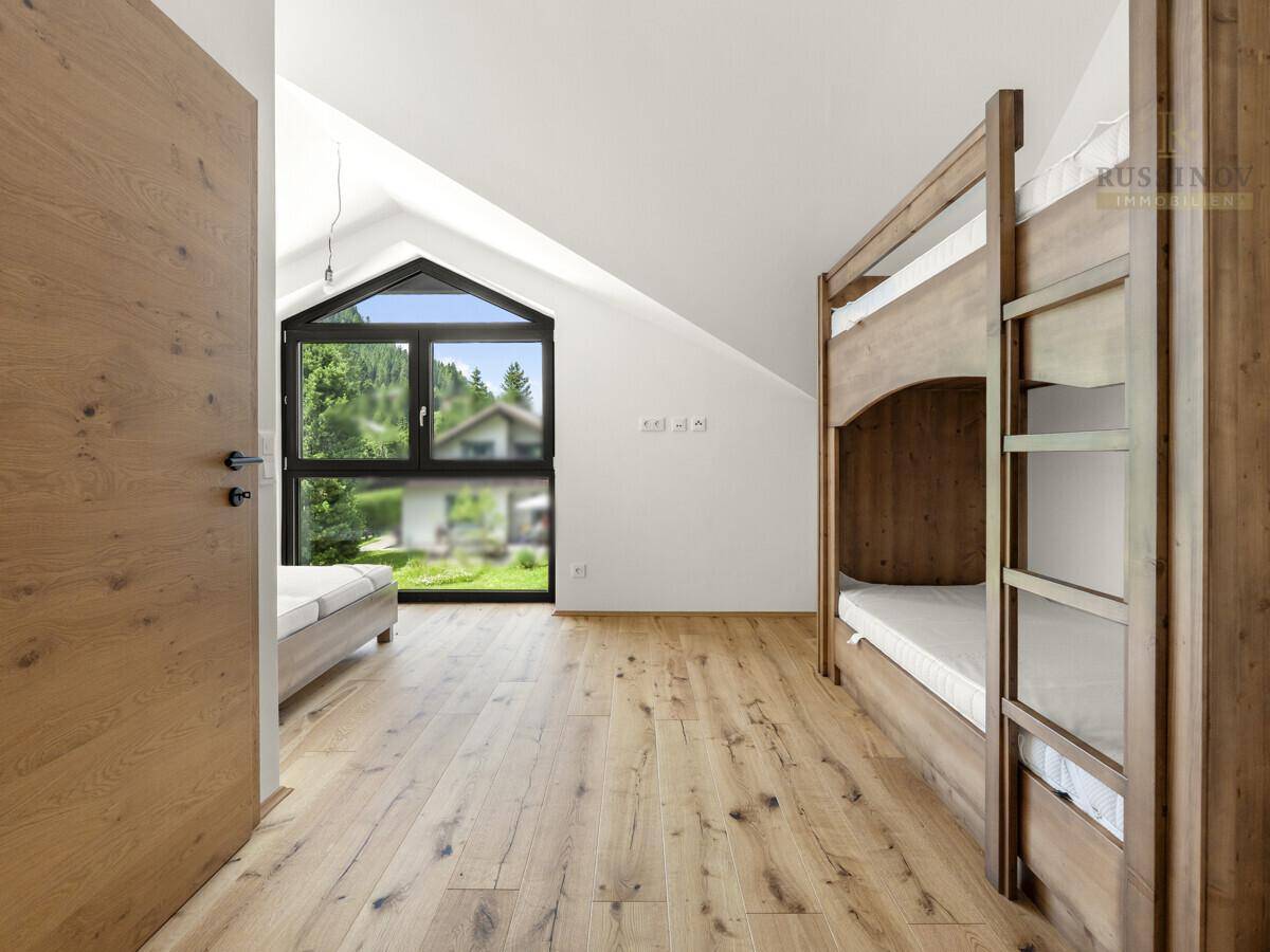 Helles Schlafzimmer mit Holzboden, Etagenbetten und großem Giebelfenster mit Bergblick.