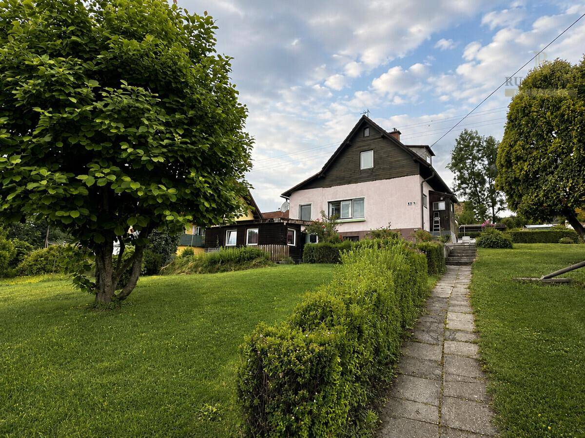 Hausansicht von der Gartenseite mit einem gepflegten Rasen, Hecke und einem Steinweg.