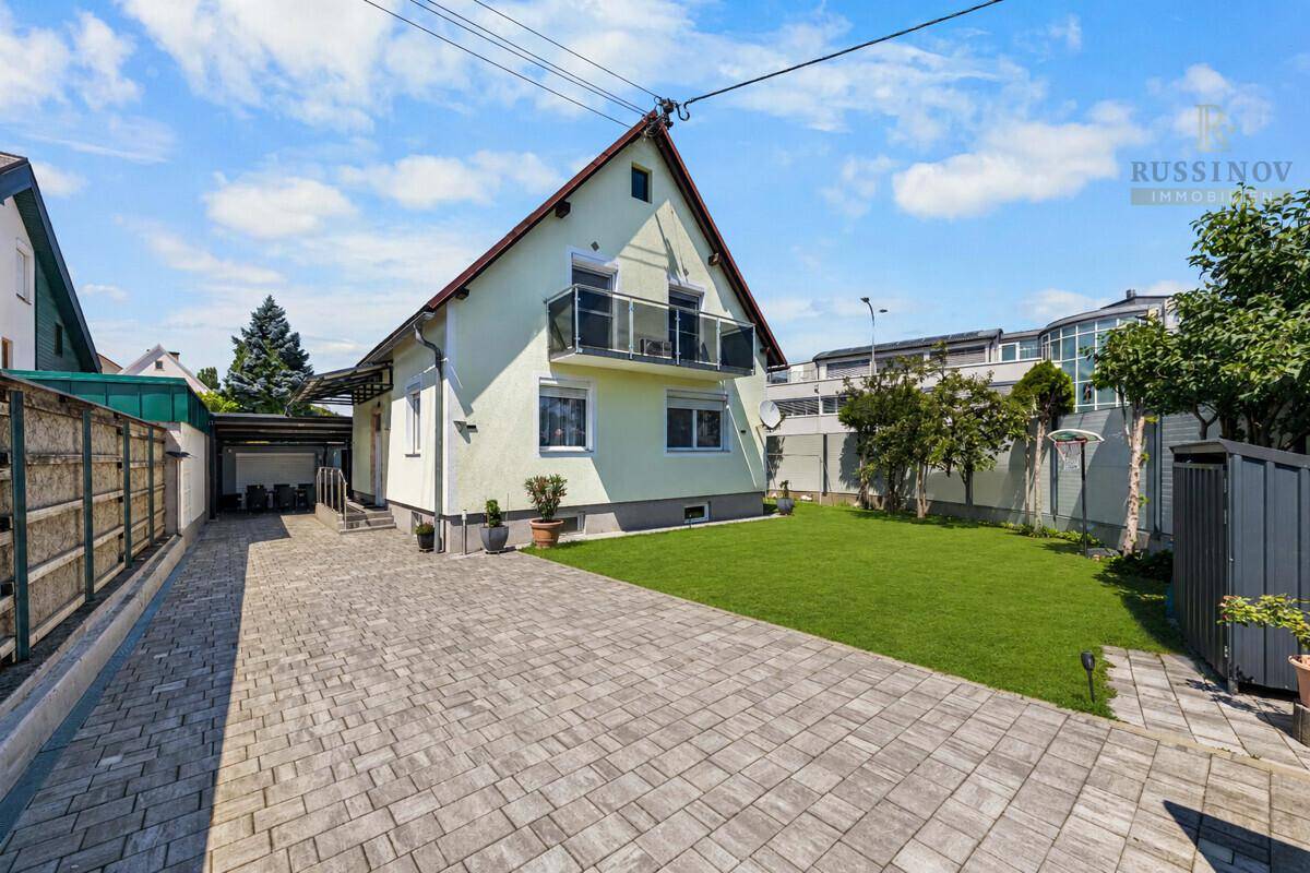 Einfamilienhaus mit gepflasterter Auffahrt, kleinem Rasenbereich und Carport.
