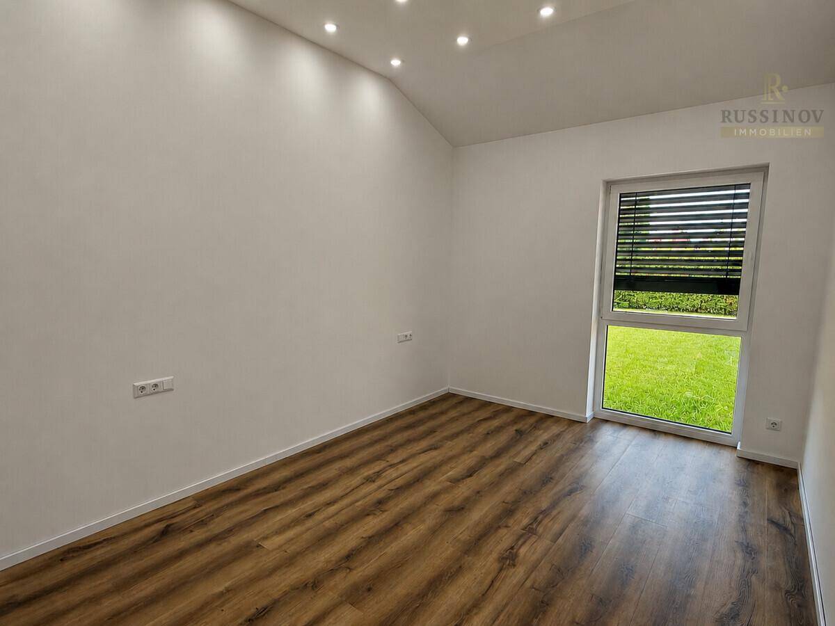Freundliches Zimmer mit Laminatboden, weiß gestrichenen Wänden und Blick ins Grüne.