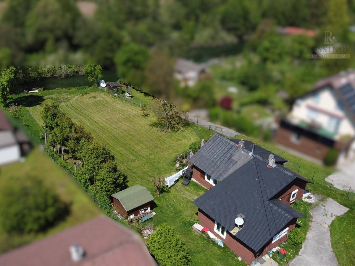 Luftaufnahme eines Anwesens mit zwei Häusern, einem Gartenschuppen und einer weitläufigen Rasenfläche.