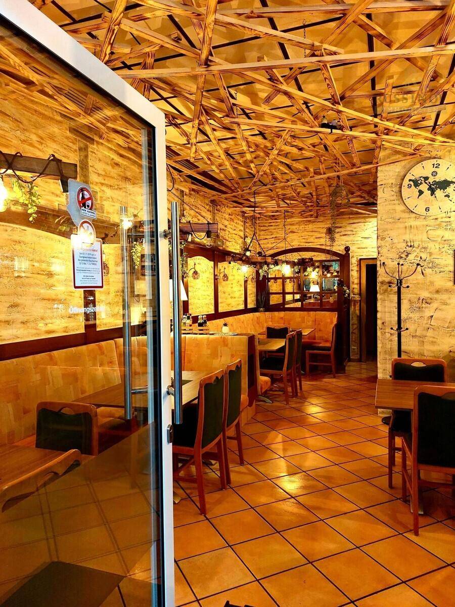 Hauptgastraum eines Restaurants mit Holztischen, gepolsterten Bänken und rustikalen Fliesenböden.