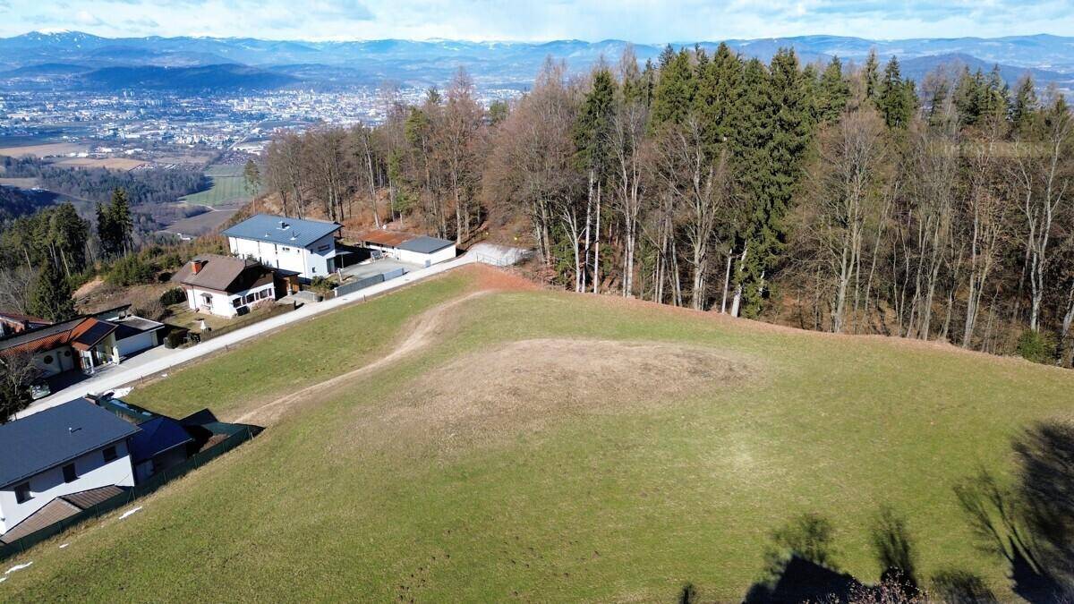 Panoramablick auf ein großes Grundstück mit mehreren Gebäuden, angrenzendem Wald und weitem Bergblick.