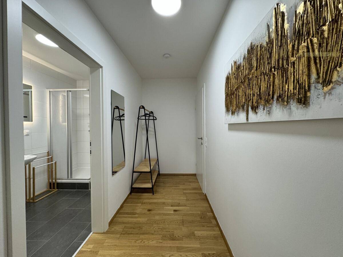 Heller Flur mit Holzboden, moderner Kunst und Zugang zum Badezimmer.