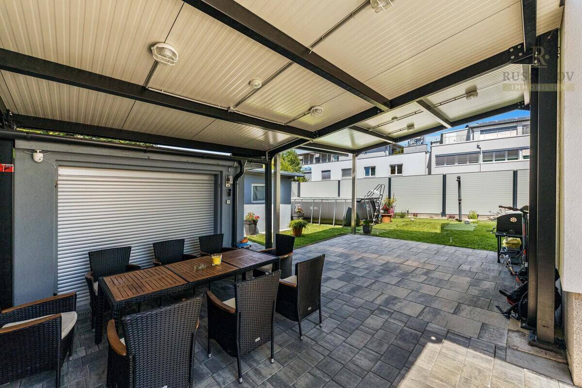Überdachte Terrasse mit Essbereich im Freien und Blick auf den Garten mit Pool.