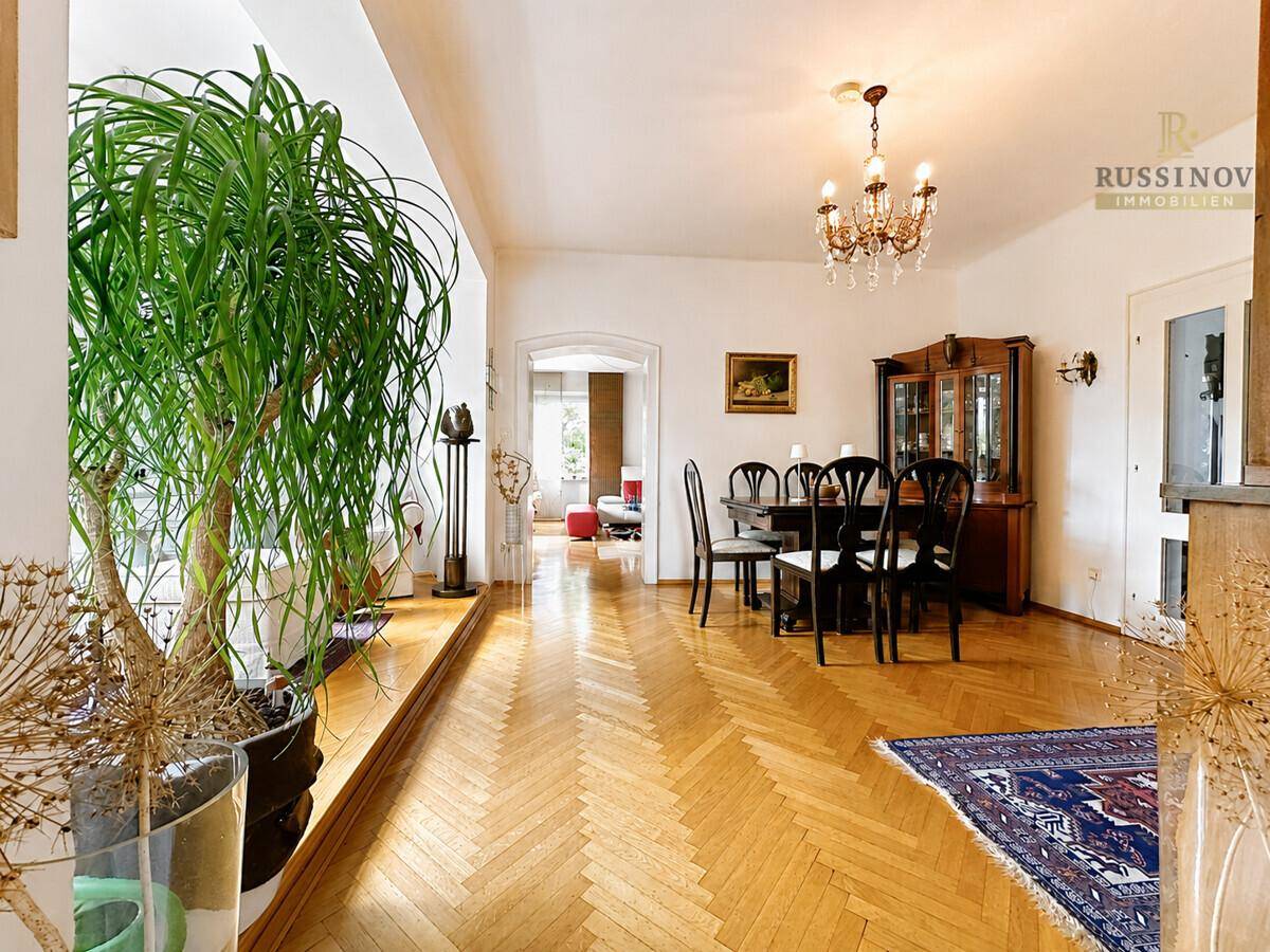 Klassischer Essbereich mit Holztisch, Stühlen und Kronleuchter, verbunden mit einem hellen Wohnbereich.